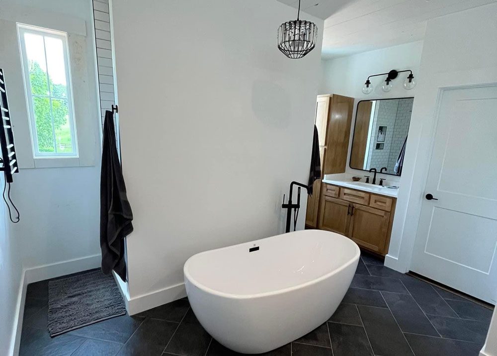 Luxury bathroom remodel with a freestanding soaking tub, wood vanity, and modern black fixtures.