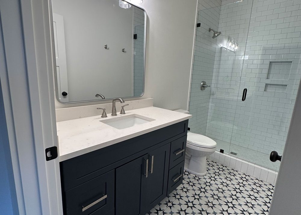 Modern bathroom remodel with navy vanity, quartz countertop, and glass walk-in shower.