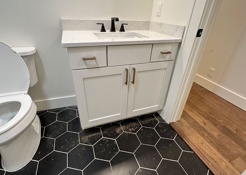 Small bathroom remodel with a white vanity, quartz countertop, and modern black hexagon tile flooring.