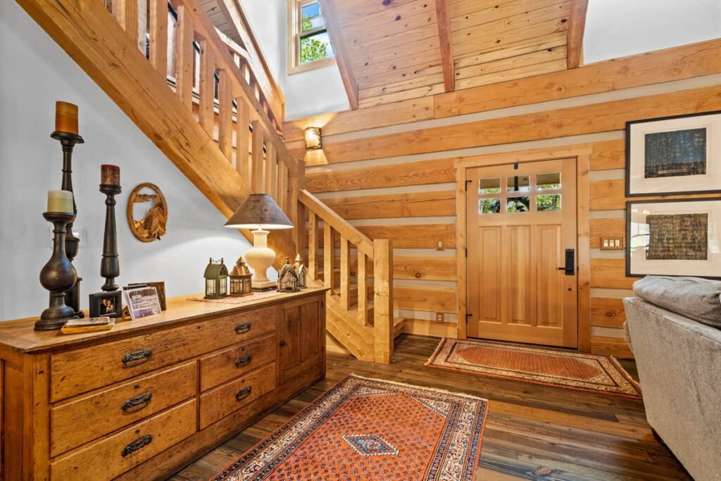 A cozy room with wooden walls, a staircase, and a wooden dresser with candles and decor.