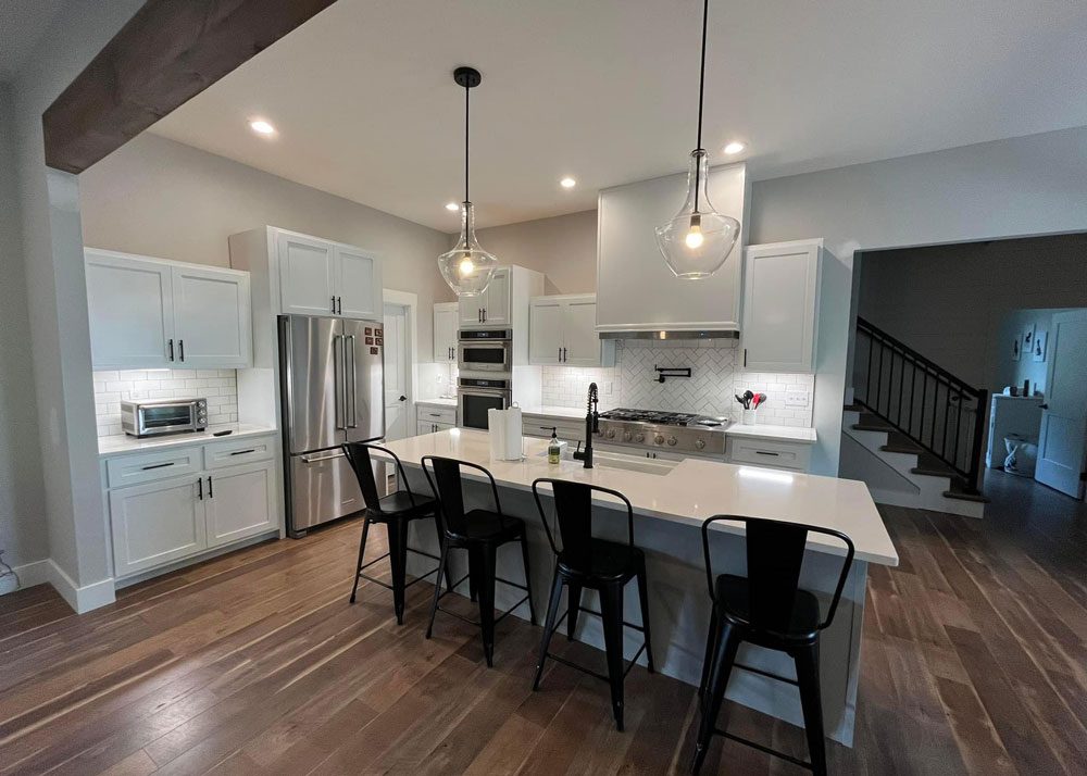 Modern white kitchen remodel with a large island, stainless steel appliances, and glass pendant lighting